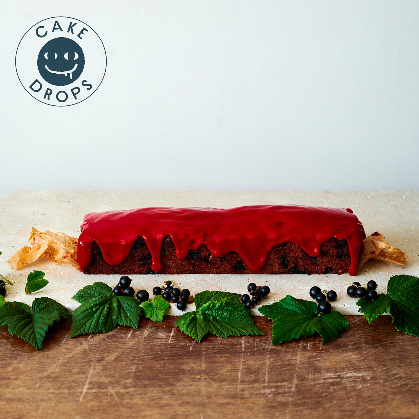 Blackcurrant Friand Loaf displayed with the leaves and berries from a blackcurrant bush.