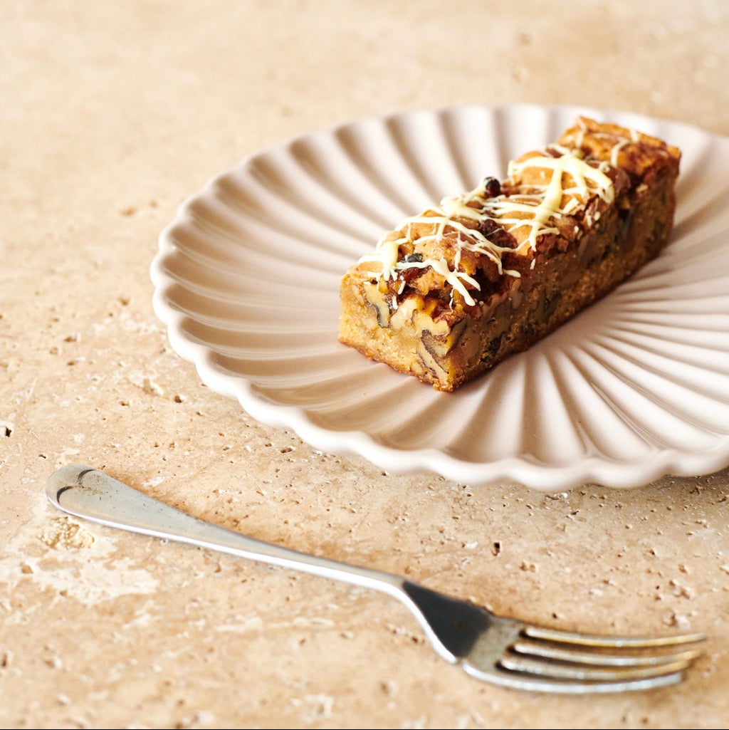 Miso Blondie with white chocolate drizzle on a decorative plate with a fork on a textured surface