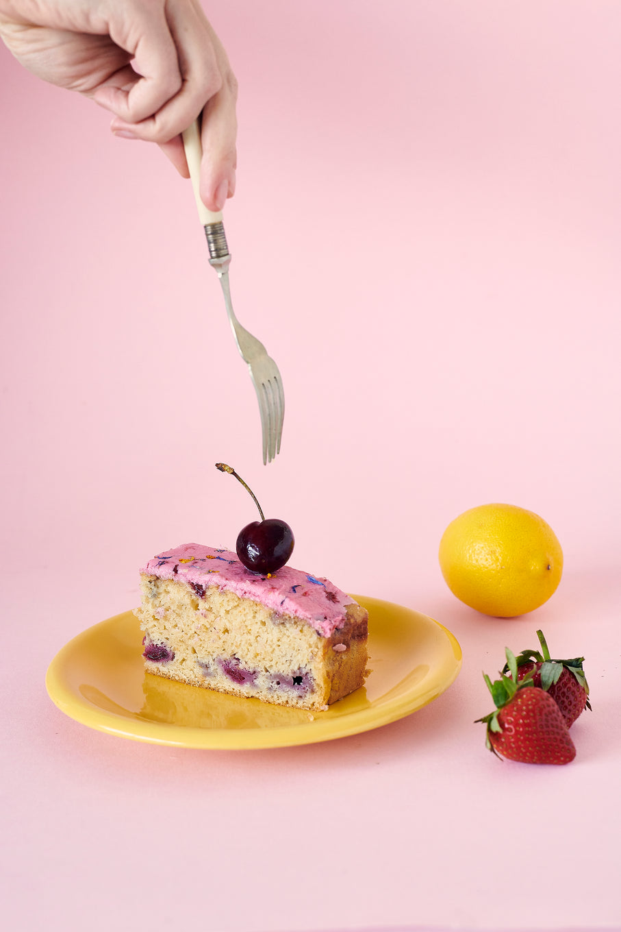 Someone Holding A Fork Above A Plated Slice Of Berry Citrus Cake