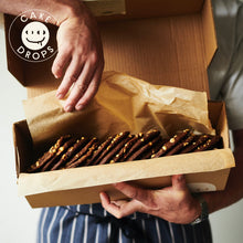 Person opening a box of Hazelnut, Miso & White Chocolate Cookies with 'Cake Drops' branding.
