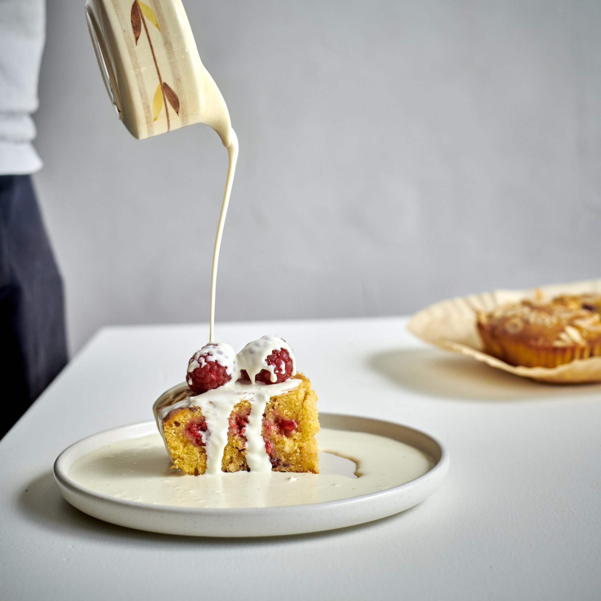 Single portion of Exploding Bakery Raspberry and White Chocolate Frangipane Cake served with cream.
